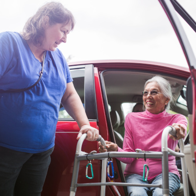 Woman helping another woman exit a car with a walker