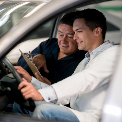 Two men in front seat of car going over paperwork on clipboard